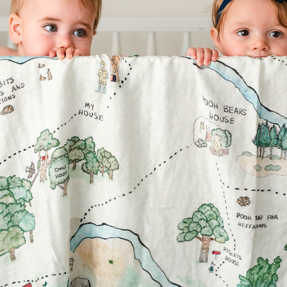 Hundred Acre Woods swaddle with babies. Winnie the Pooh map themed swaddle blanket babies in crib.