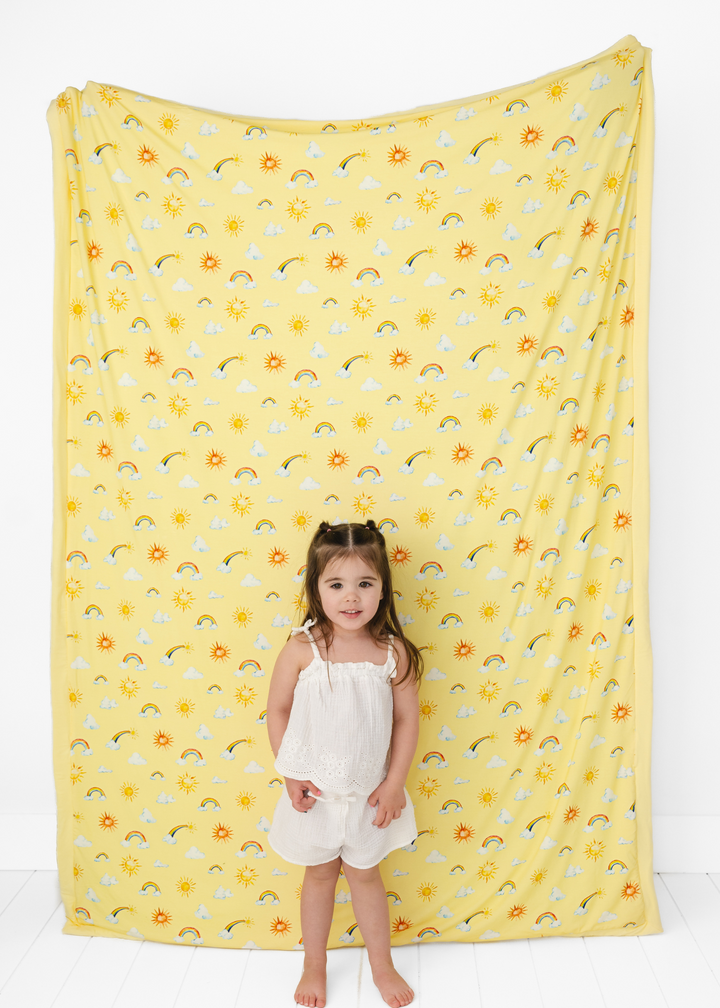 Sunshine and rainbow big bamboo quilt, yellow in color, modeled with a toddler. Perfect gift for a rainbow baby shower.