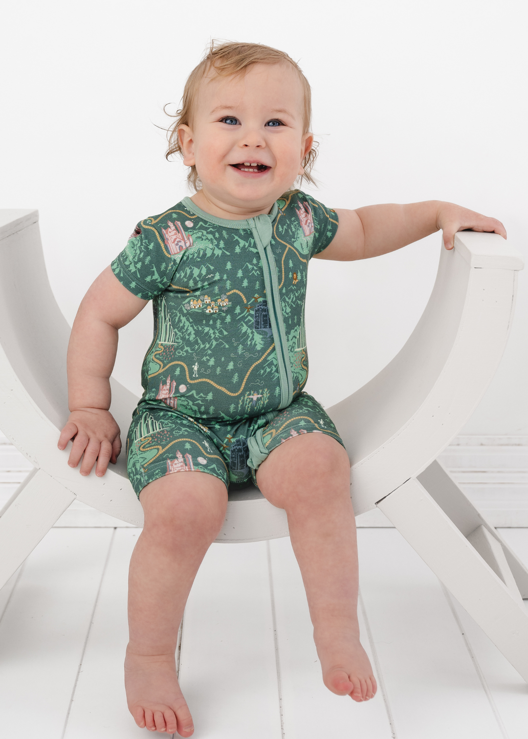 Short sleeve romper in our Emerald City design, inspired by the Wizard of Oz with a deep green background, yellow brick road, and Wizard of Oz characters.