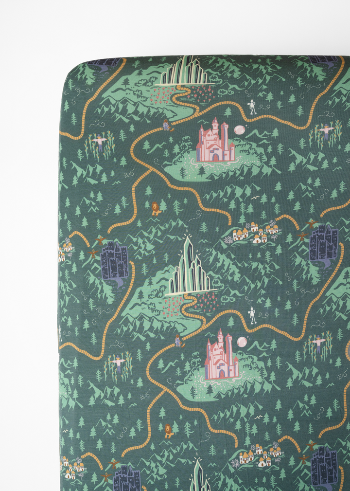 A crib sheet with a green background featuring illustrations of characters and scenes from the Wizard of Oz. Emerald City crib sheet. 