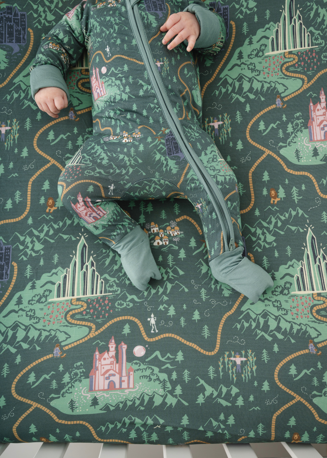 A close up picture of a crib sheet inspired by the Wizard of Oz. This crib sheet features a deep green background with a yellow brick road running throughout and Wizard of Oz characters.