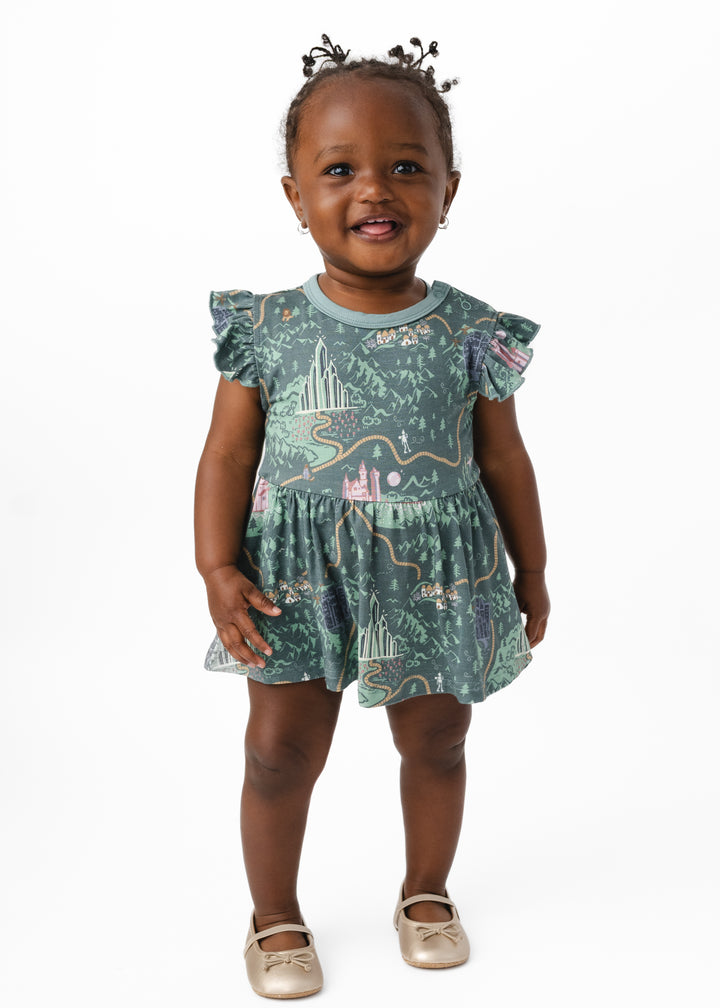 A baby wearing a Wizard of Oz inspired short sleeved dress. The design features Wizard of Oz characters, Emerald City, yellow brick road, and more!