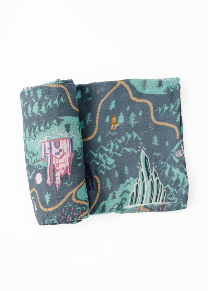 A swaddle blanket with a vibrant green tone featuring a whimsical pattern with characters and a landscape inspired by the Emerald City.