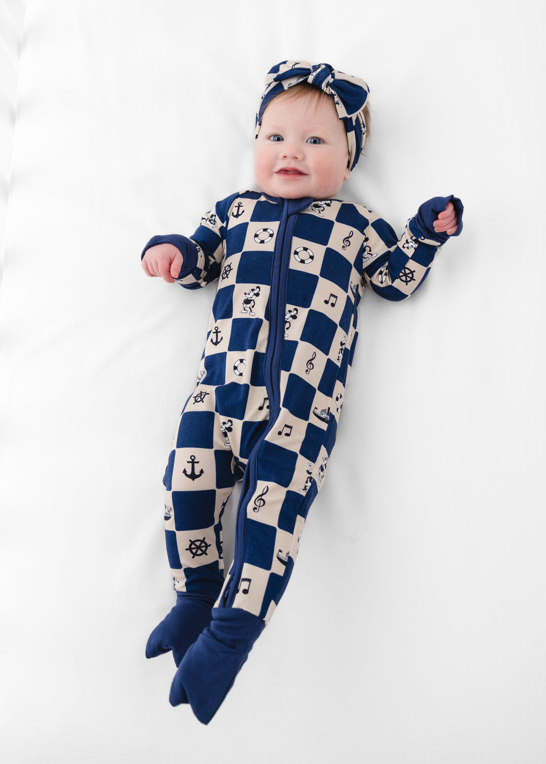 Baby wearing a blue and white checkered onesie with nautical patterns on a white background featuring Steamboat Willie. Steamboat Willie Bamboo Zip Sleeper.