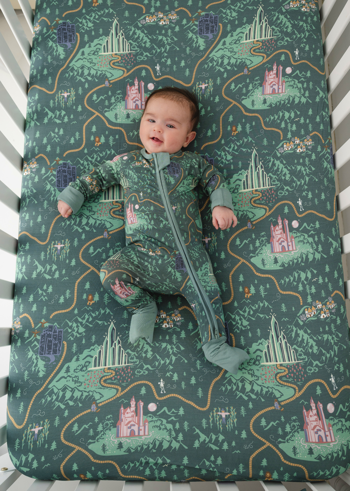 A crib sheet and bamboo in a Wizard of Oz inspired design on a green background with a yellow brick road and Wizard of Oz characters. 