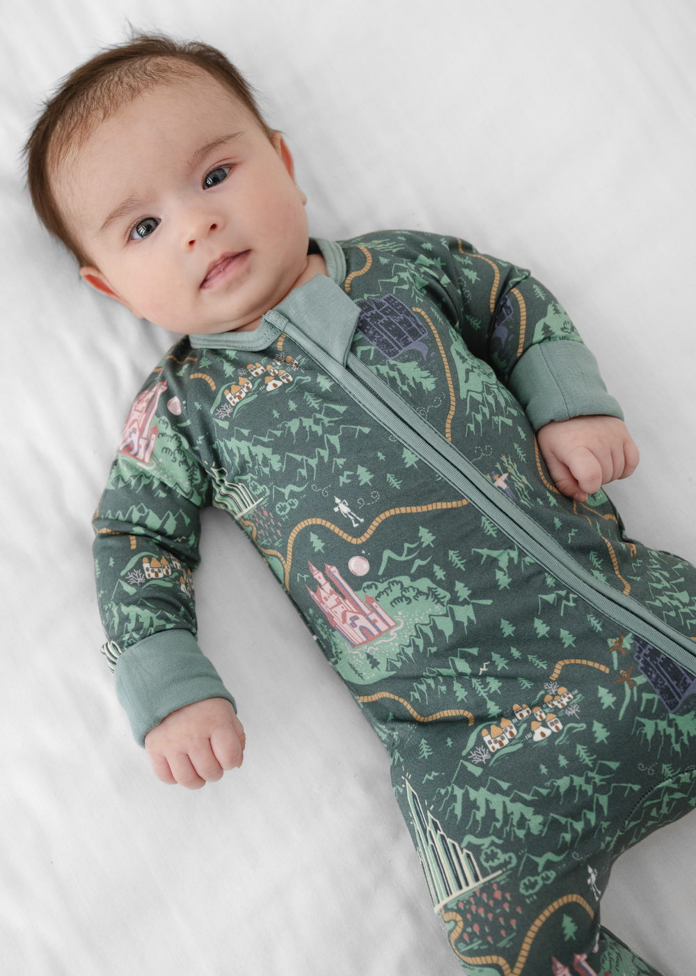 A baby wearing a Wizard of Oz inspired sleeper with a deep green background and Wizard of Oz characters and a yellow brick road.