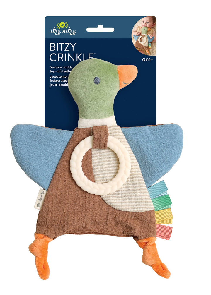 A duck-shaped baby teething toy by Desi Desi, featuring a green head, blue wings, a brown apron, and orange feet, with a cream ring and colorful tabs. It is shown with its dark blue cardboard packaging header card on a plain white background.